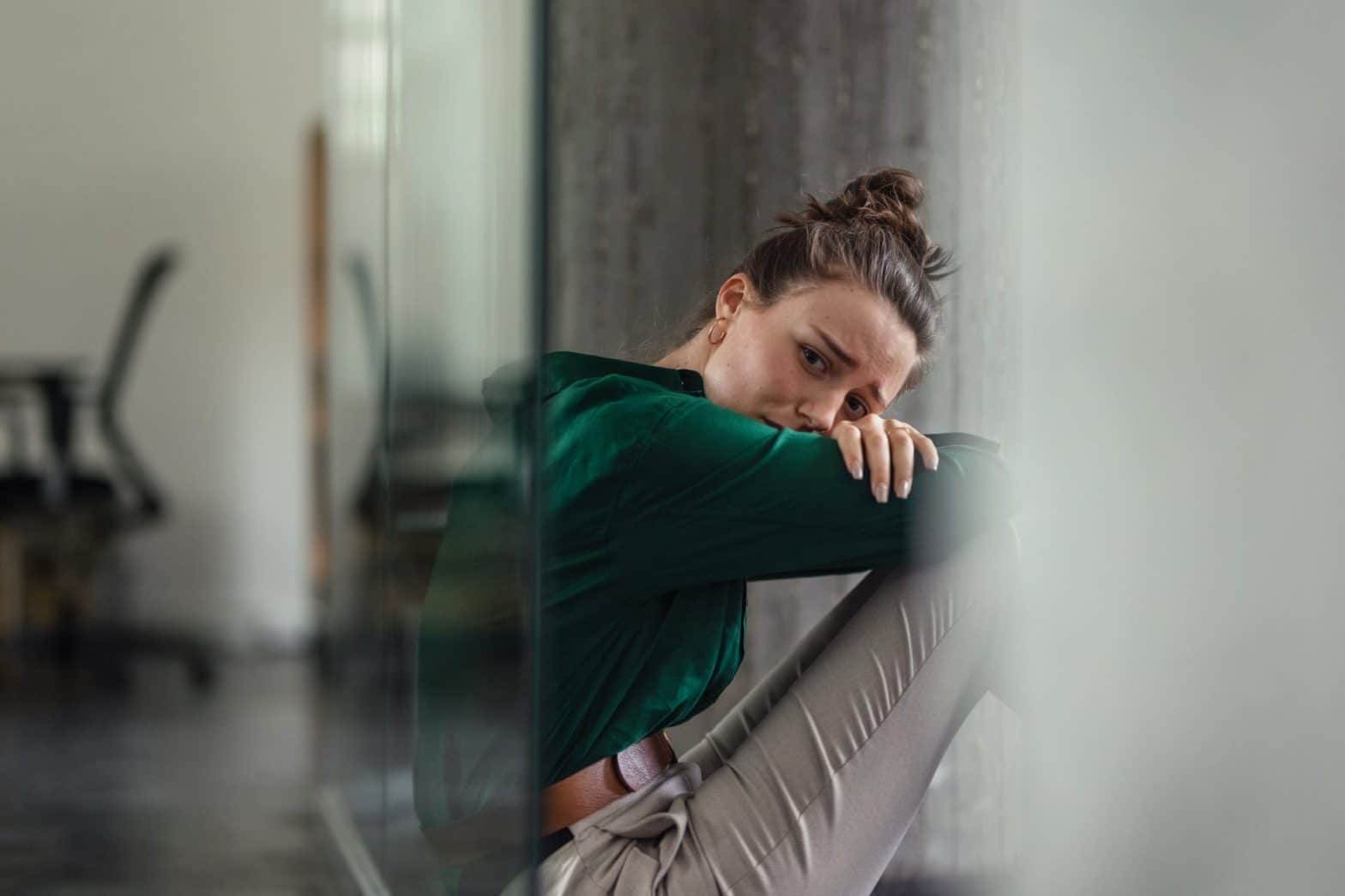 Woman sitting on the floor sad next to a computer chair