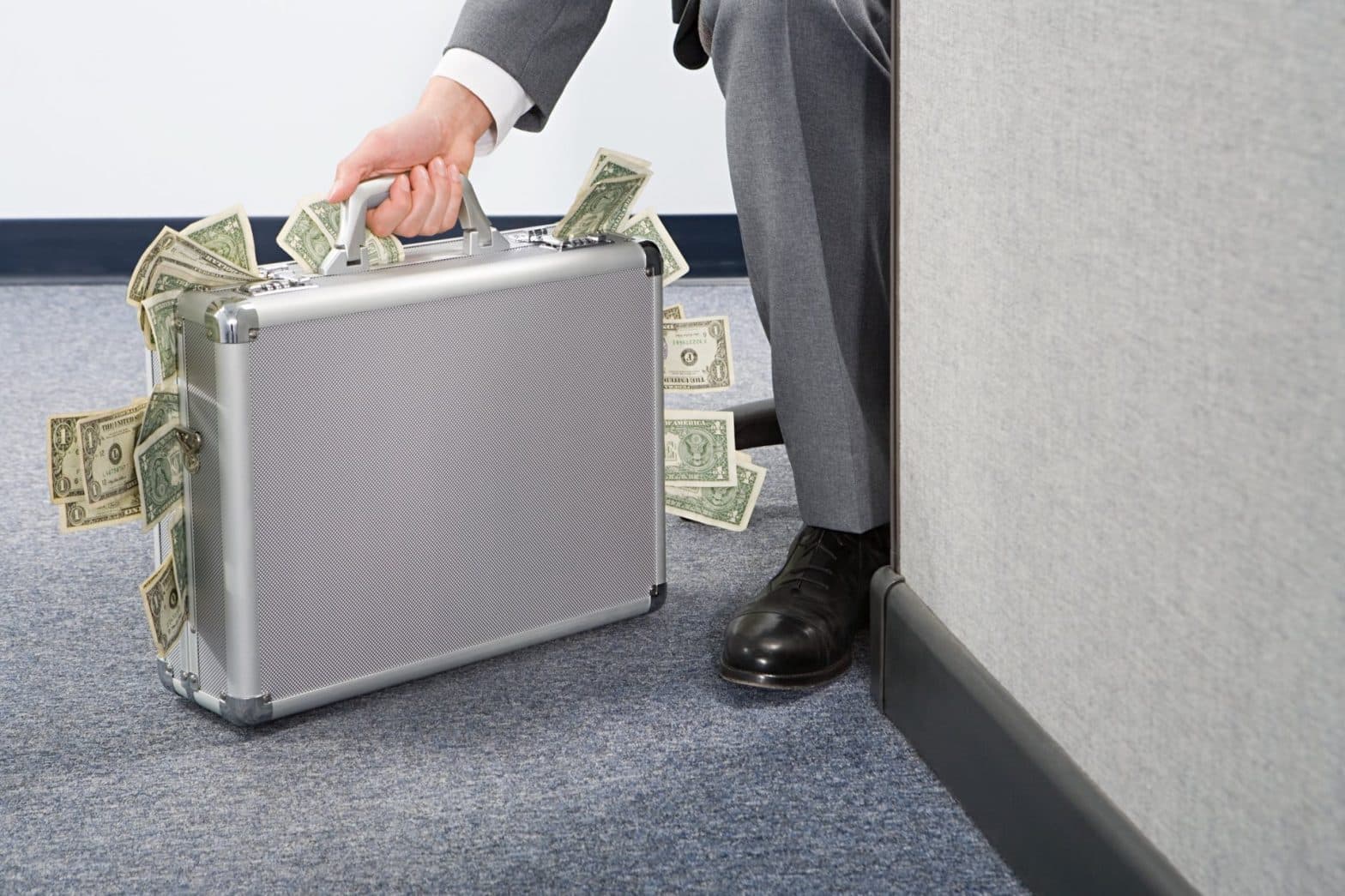 A person hiding behind a wall in a grey suit holding a brief case with money coming out of it