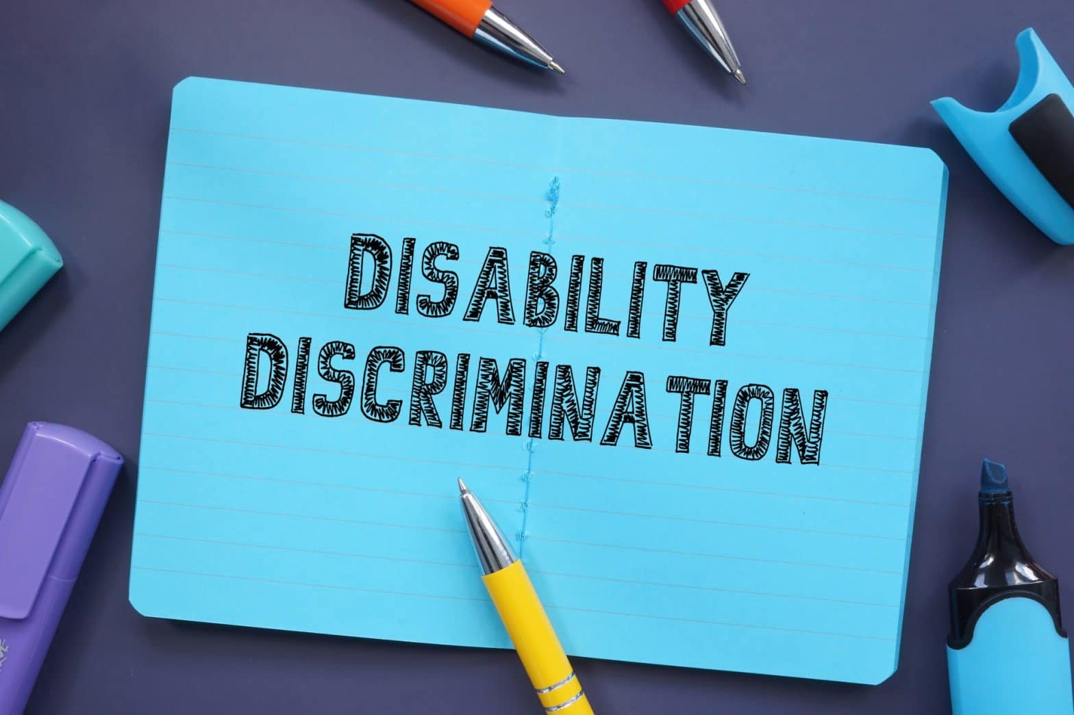 Disability Discrimination on a blue notepad with pens nearby