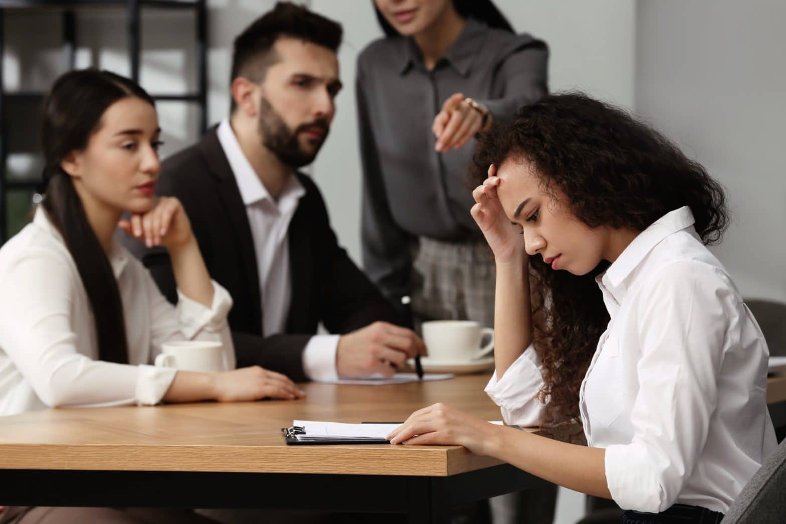 Four people sitting at a desk with one person singled out
