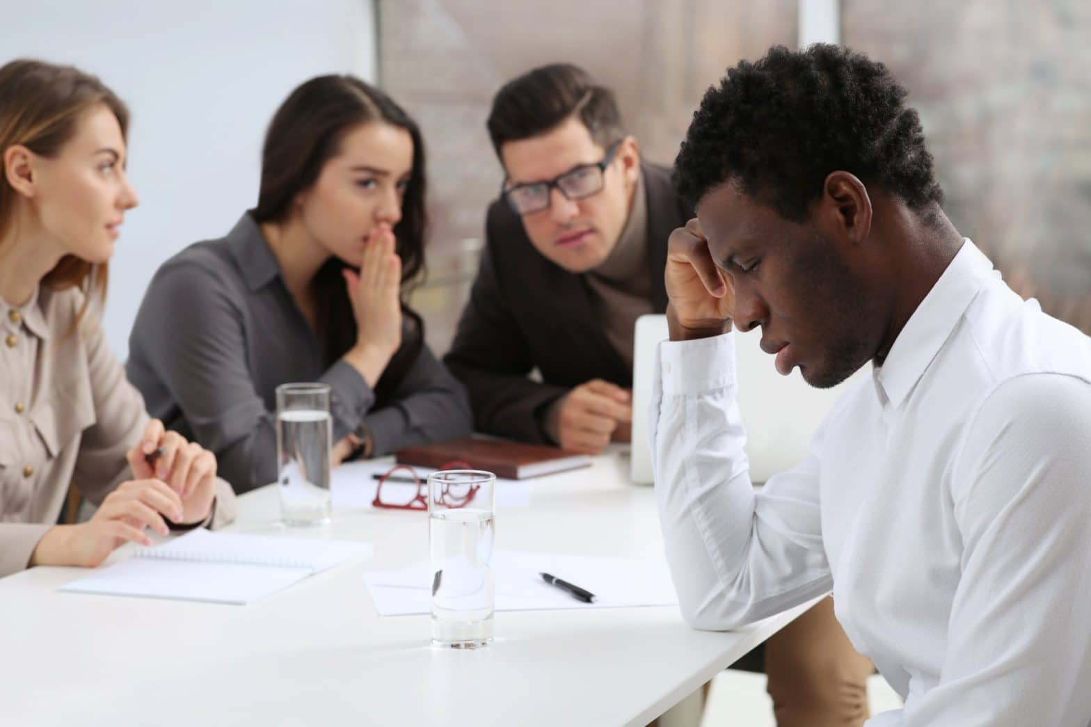 Four people sitting at a desk together with three people huddled up talking about the other