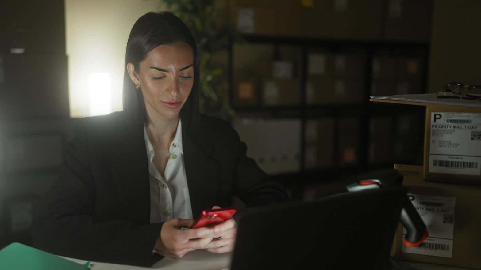 A person sits in a darkened office looking at a red cell phone.